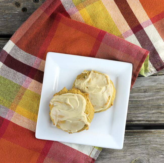 Pumpkin cookies on a white plate on top of a plaid napkin.