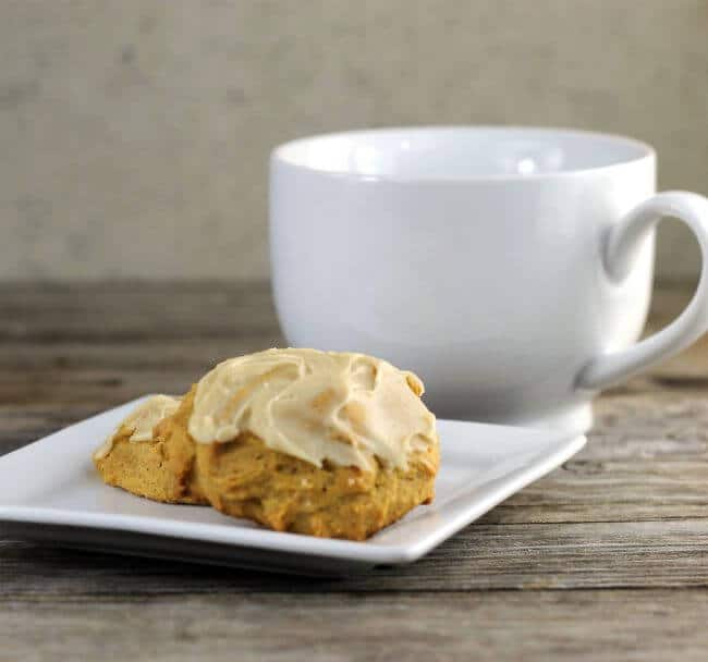 Pumpkin cookies on a white plate with a white coffee cup behind.