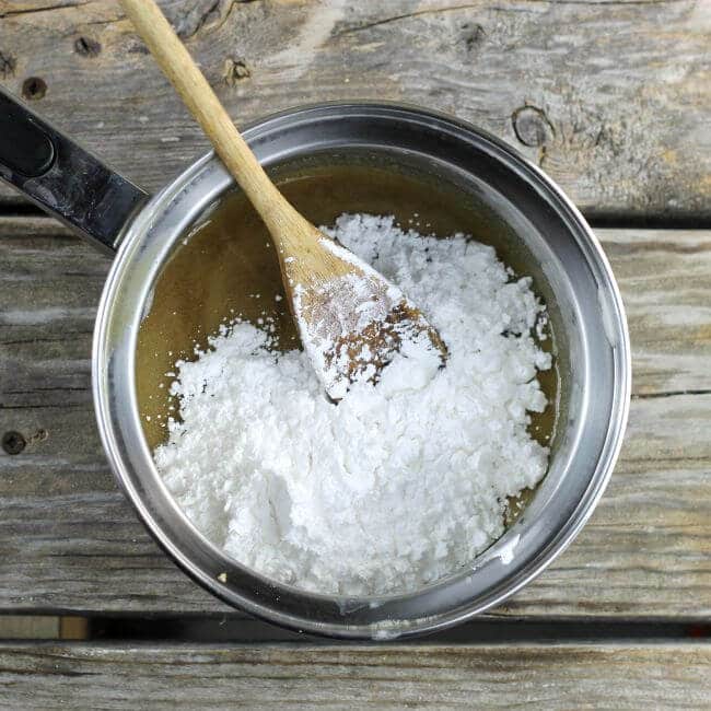 Powdered sugar added to frosting in a sauce pan with wooden spoons