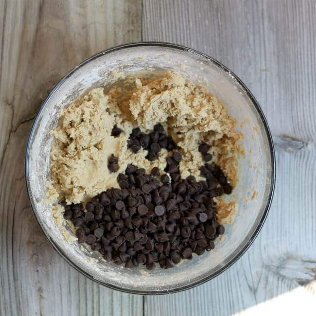 Chocolate chips added to cookie dough in a glass bowl.