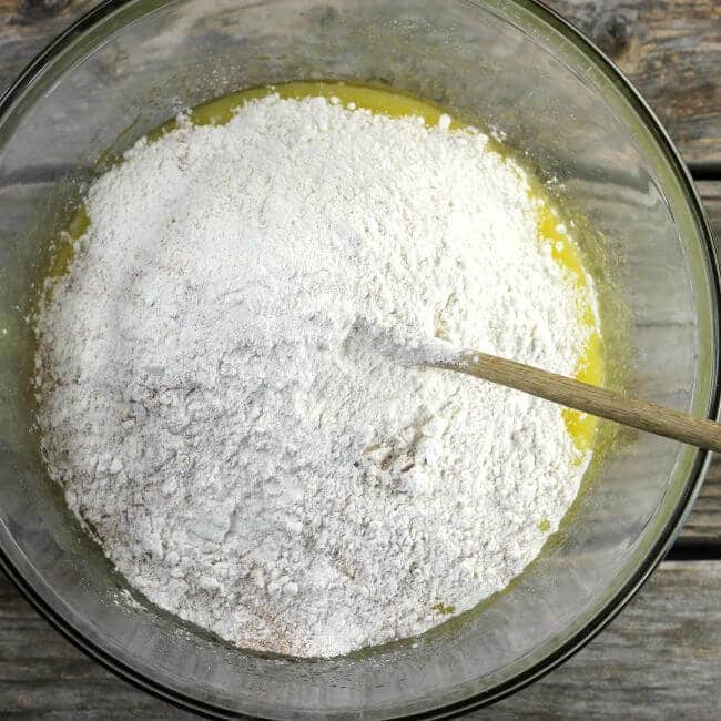 Flour is add to the egg mixture with a wooden spoon in the bowl.