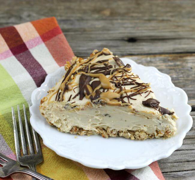 Slice of peanut butter pie on a white plate sitting on a plaid napkin with forks
