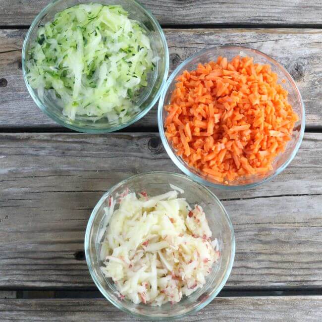 Shredded zucchini, carrots, and apple in small bowls.
