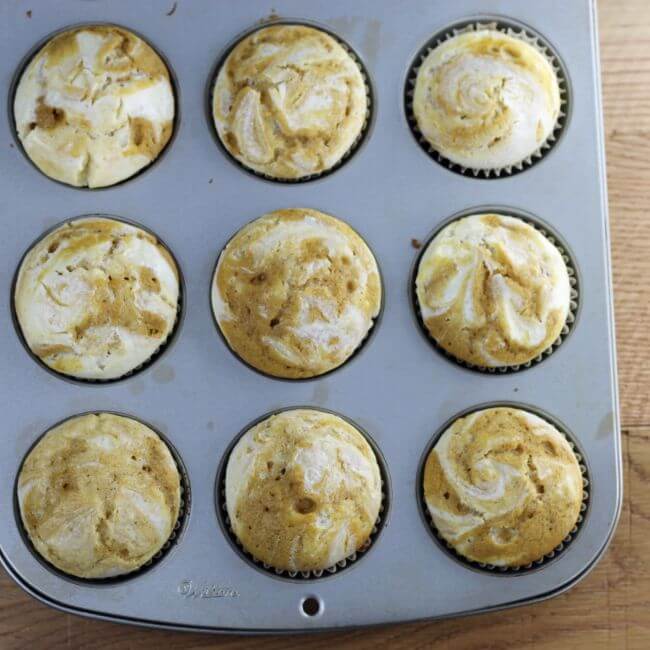 Baked pumpkin cream cheese cupcakes in a muffin tin.