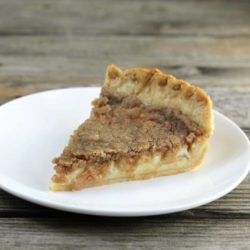 Side angle view of a slice of apple sour cream pie on a white plate.
