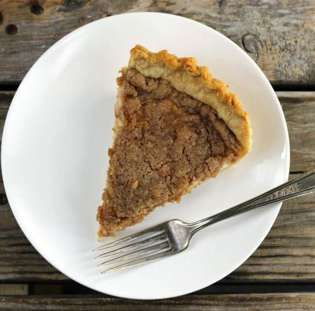 Looking down at a slice of apple pie on a white plate with a fork on the side.
