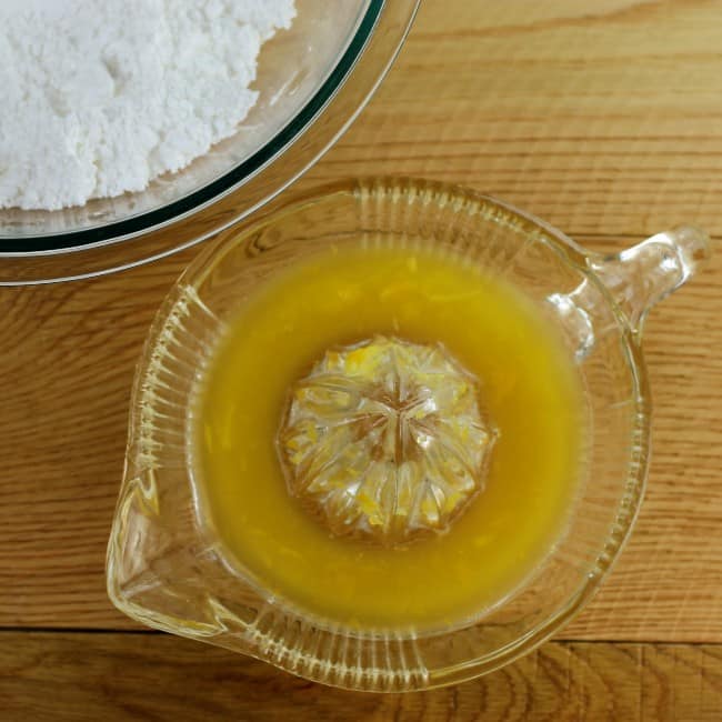 Orange juice in a glass bowl with a bowl of powdered sugar.