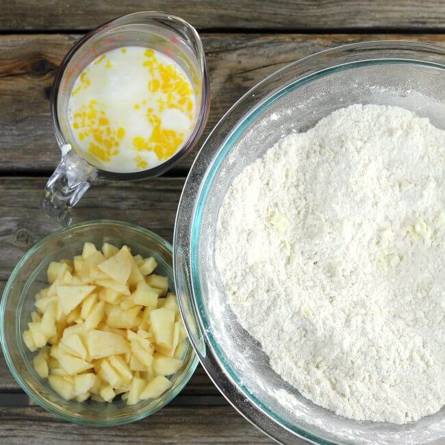Flour mixture in a bowl with chopped apples and the milk mixture next to it.