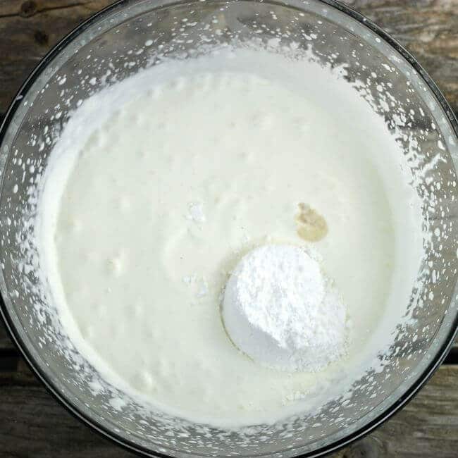 Powdered sugar, and vanilla added to whipping cream in a bowl.