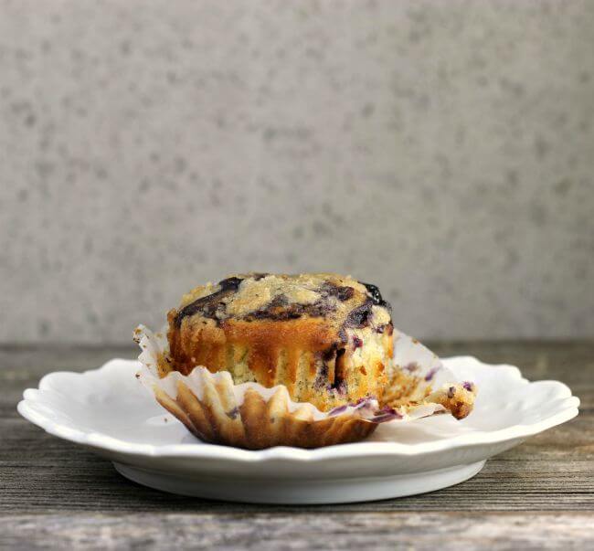 unwrapped blueberry muffin on a white plate