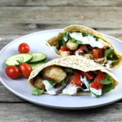 A pita stuffed with chicken, tomato, and lettuce with cherry tomatoes and cucumber on the side.