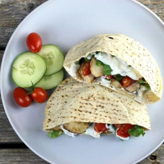 A Pita stuffed with tomato, chicken, and lettuce with cucumber and cherry tomatoes on the side.