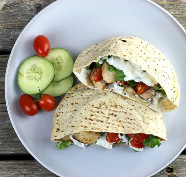 A Pita stuffed with tomato, chicken, and lettuce with cucumber and cherry tomatoes on the side.
