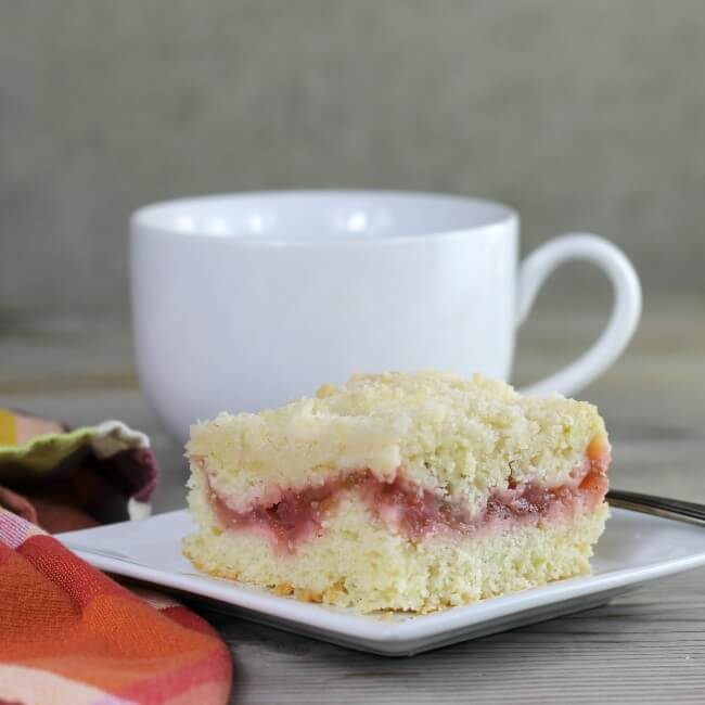 Side view of a slice of coffee cake with a mug behind the plate.