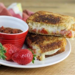 Side view of pizza grilled cheese with strawberries and a bowl of pizza sauce on a white plate.