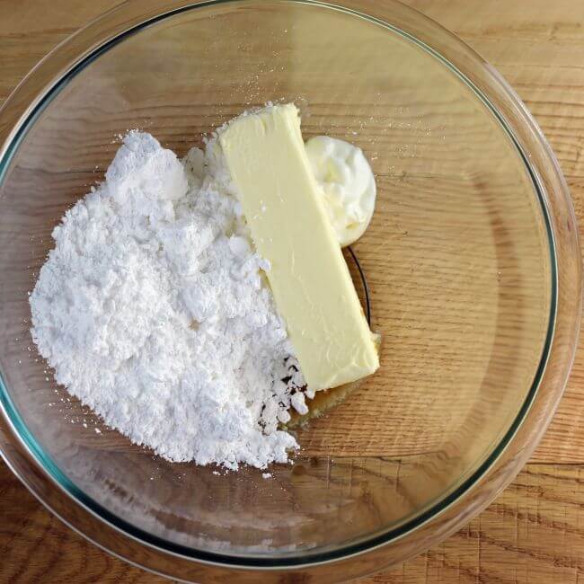 Powdered sugar, butter, and vanilla are added to a glass mixing bowl.