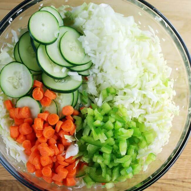 Cabbage, cucumbers, carrots, green pepper, and onion in a large bowl.