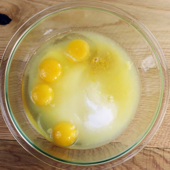 A glass bowl of eggs, lemon zest, lemon juice, sugar, and flour.