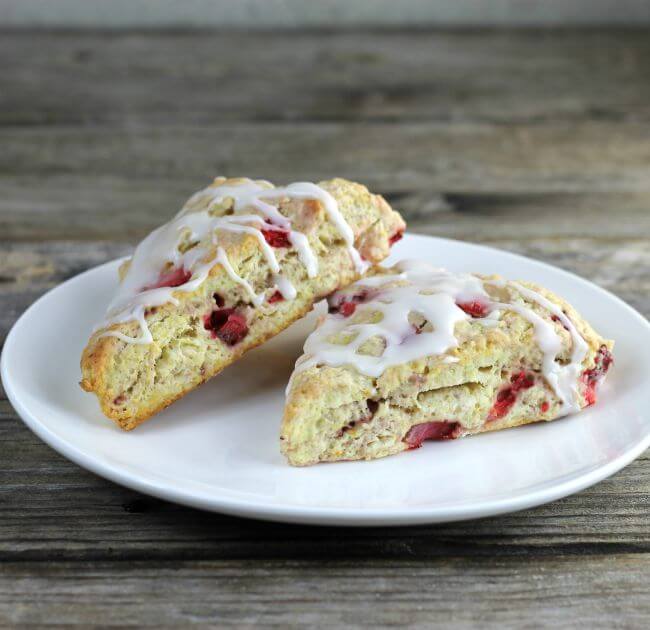 Side angle view of two lemon strawberry scones on a white plate.