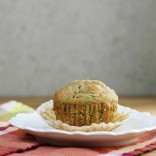 The side view of a zucchini muffin on a white plate with a napkin under the plate.