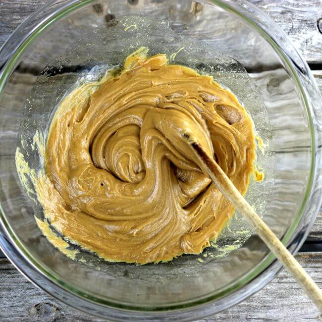 Peanut butter and honey blended together in a bowl with a wooden spoon.