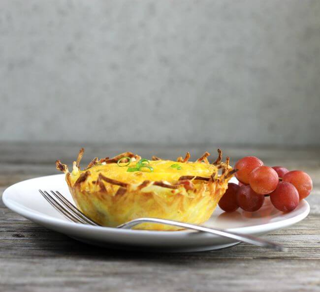 Side view of an egg cup on a white plate with grapes on the side.