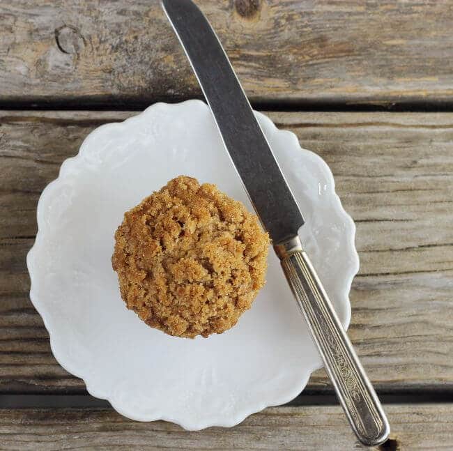 Looking down at a muffin on a white plate with a knife on the side.