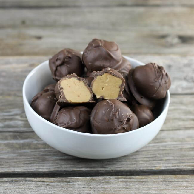 Peanut butter balls in a white bowl with one of the balls cut in half.