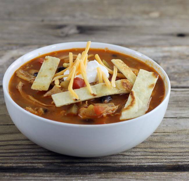 Side angle view of southwest soup with sour cream, tortella strips, and cheese on top.