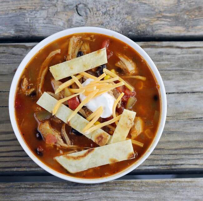 Overhead view of a bowl of southwest soup with cheese tortilla strips and sour cream on top.