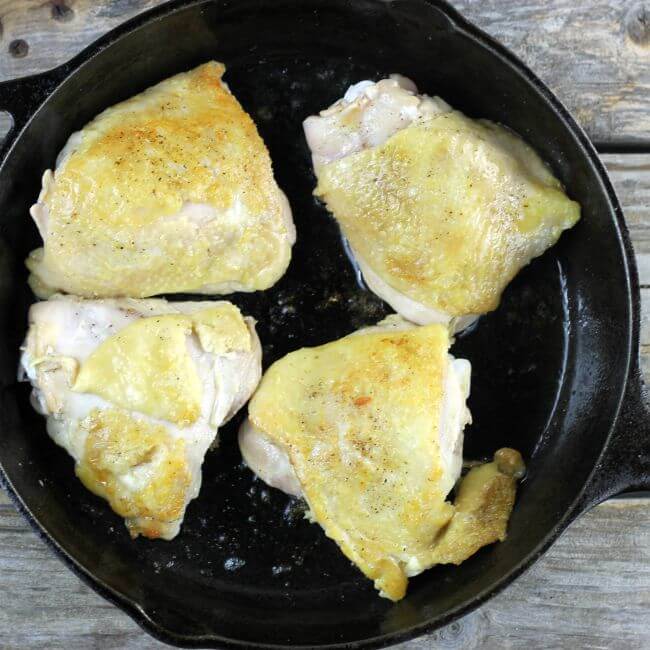 Four chicken thighs in a skillet.