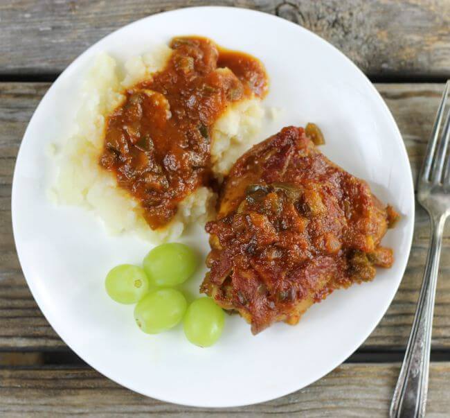 Looking down at a white plate with one piece of chicken, mashed potatoes and sauce, and green grapes.