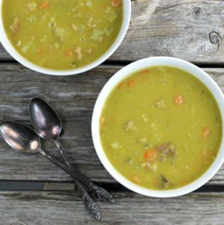 Two bowls of split pea soup in white bowls with spoons on the side.