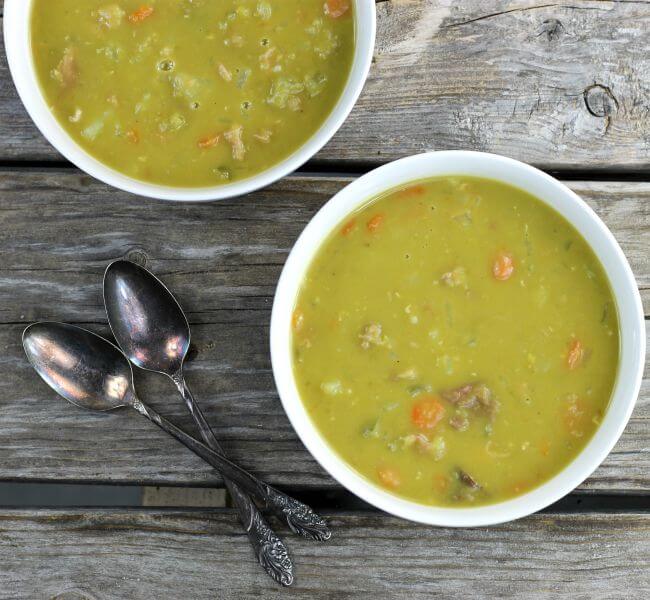 Two bowls of split pea soup in white bowls with spoons on the side. 