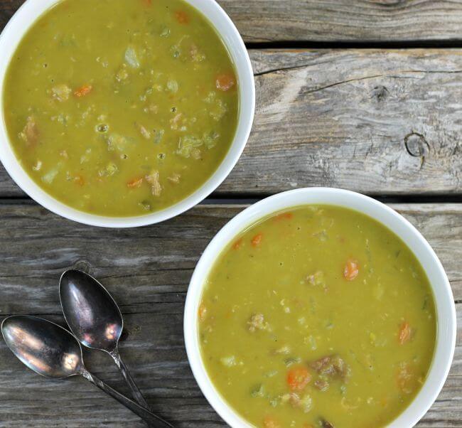 Two bowls of split pea soup with two spoons on the side.