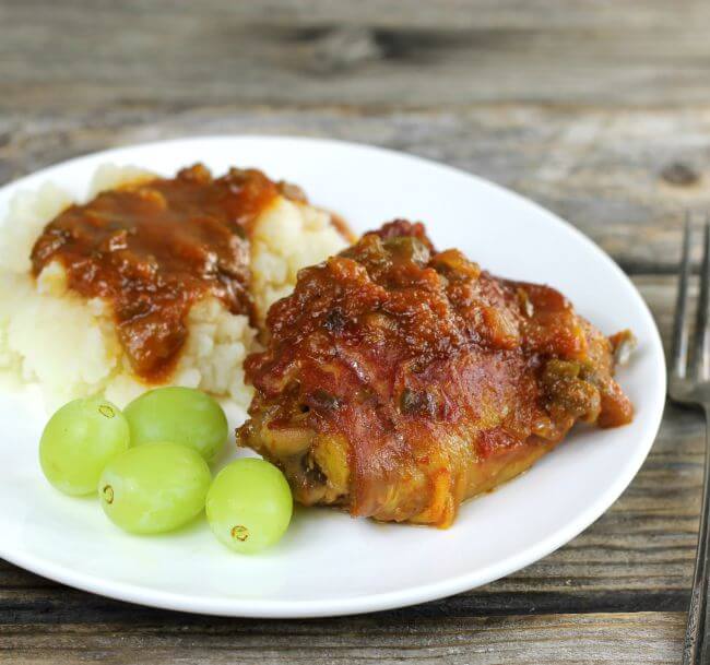 Side angle view of saucy chicken with potatoes and green grapes.