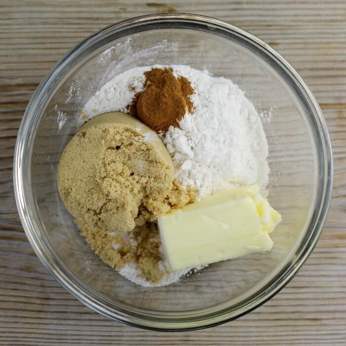 Brown sugar, sugar, flour, cinnamon, and butter are added to a bowl.