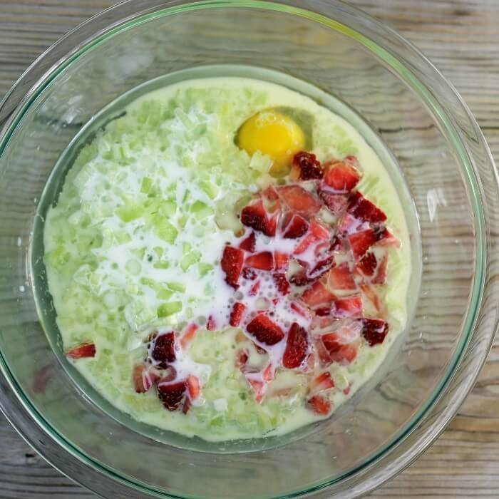 Rhubarb, strawberries, egg, oil, and milk added to a mixing bowl.