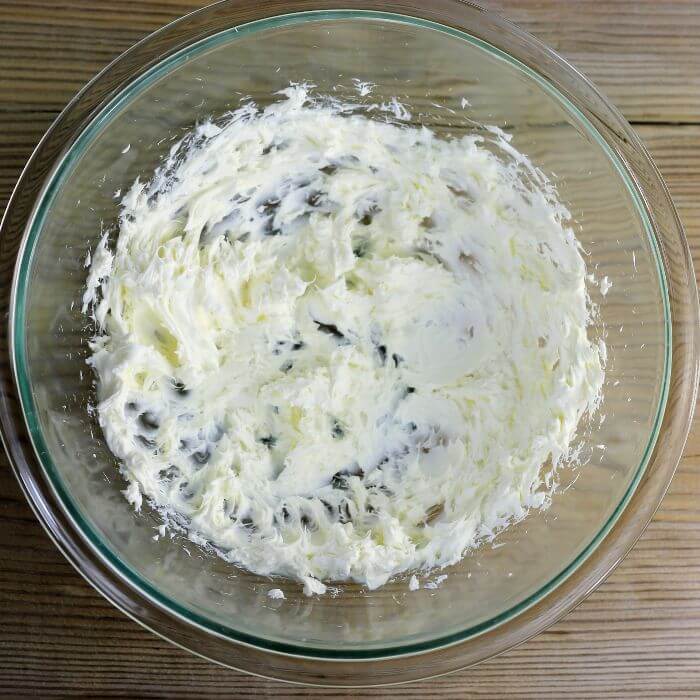 Cream cheese is beaten until fluffy in a bowl.