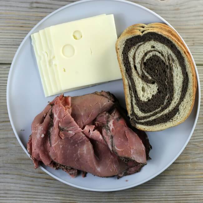 Pastrami, Swiss cheese, and bread on a gray plate.