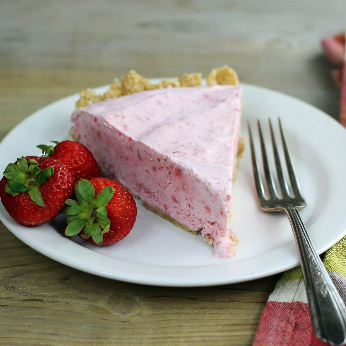 A sode angle view of a piece of strawberry pie with a strawberries and a fork on the sides.