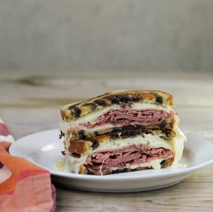 Side view of a pastrami sandwich on a white plate.