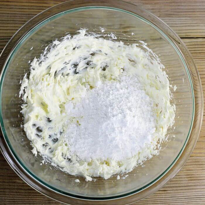 Powdered sugar is added to the cream cheese in the bowl.
