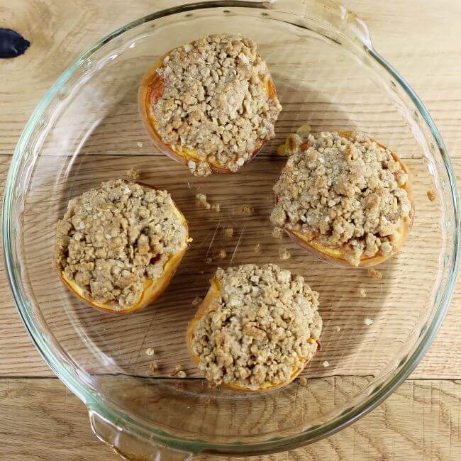 Baked peached with crumble topping in a glass dish.