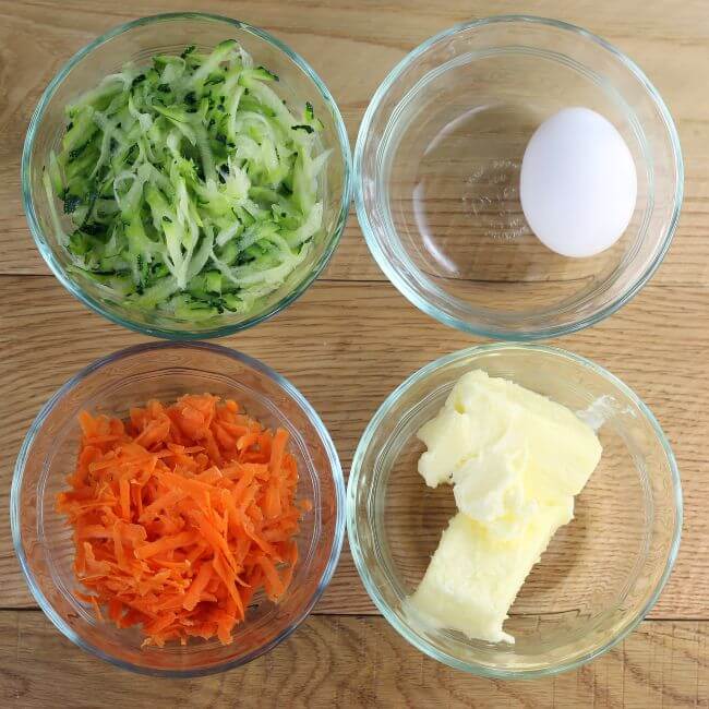 Bowl with shredded zucchini, shredded carrots, an egg, and butter.