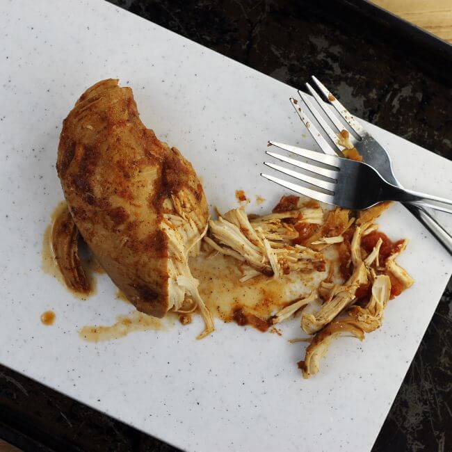 Shredding chicken breast on a cutting board with two forks.