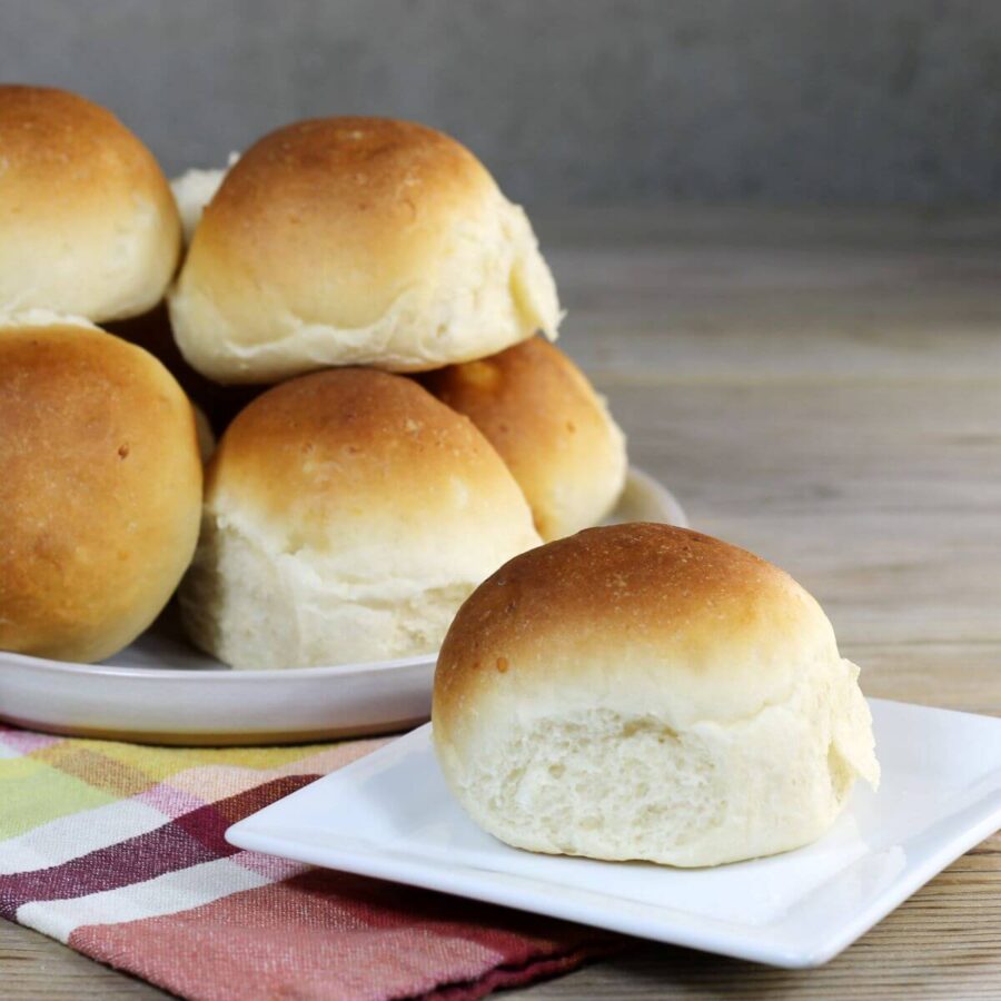 A side view of a bun on a white plate with pile of buns on a plate in the back.