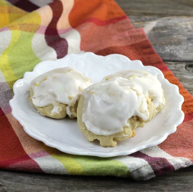 Three frosted cookies on a white plate sitting on a plaid napkin.
