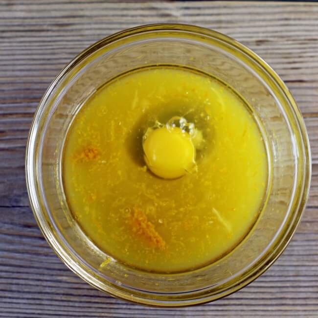 An egg, orange juice, zest, and oil are added to a bowl.