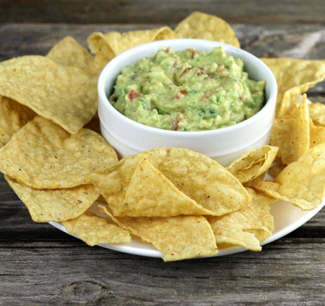 Avocado guacamole in a white bowl with chips on the side.